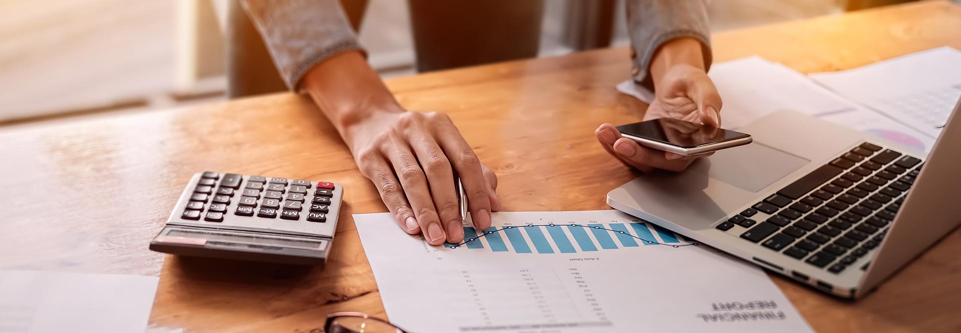 Closeup of a person looking at graphs and their cell phone at their desk