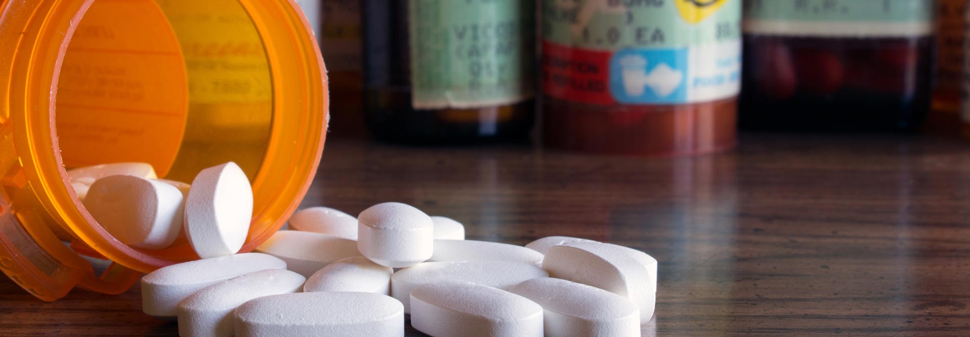 Pills spilling out of a prescription bottle in front of other prescription bottles